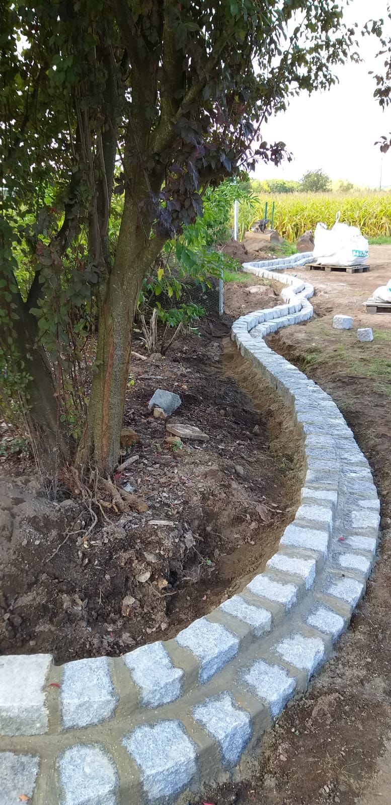 Geschwungene Beetumrandung mit Natursteinen im Bau